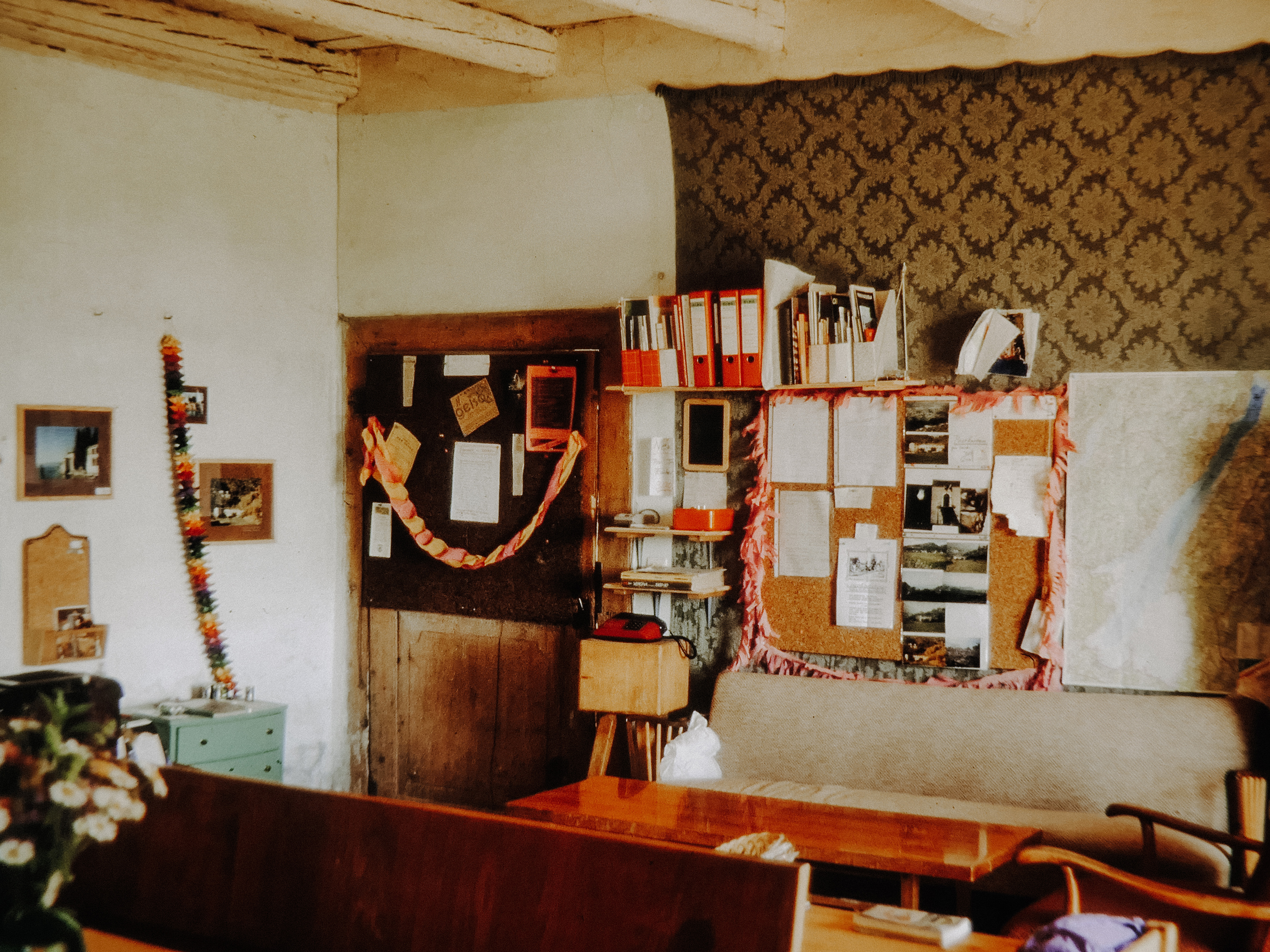 Blick in die Küche mit Girlanden, Ordnern und einer vollen Pinnwand – davor eine Sitzgruppe und Blumen